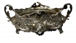 Antiga floreira de mesa em metal espessurado a prata apresentando corpo ovalado vazado assentado sobre pés estilizados, com duas alças laterais integradas e rica decoração em alto-relevo. Medidas: 31 x 18,5 x 12 cm
