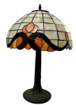 Tiffany Style. Antigo e imponente abajur de mesa em metal com pátina, em estilo Art Nouveau e cúpula em vitral confeccionada pela técnica Tiffany, composta por vidros opalescentes em tons de branco, âmbar, laranja e preto, unidos por solda de estanho, com decoração floral estilizada. Funcionando. Medidas: 55 x 40,5 cm.