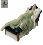 Royal Doulton - Escultura em porcelana esmaltada e policromada, modelo "Sleeping Beauty", HN 3079, concebida por Adrian Hughes e lançada em 1987. Representa figura feminina reclinada sobre chaise longue, com rica modelagem das vestes e delicada policromia em tons de verde, creme e preto. Manufatura na base. Medidas: 9 x 21 x 11,5 cm.