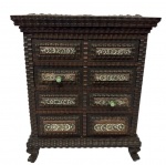 Mini cômoda porta-joias em madeira ricamente entalhada, com oito gavetas ornamentadas por aplicações em prata com decoração floral em relevo e puxadores em pedra verde. Base e molduras recortadas. Ausência de seis puxadores. Medidas: 24,5 x 19 x 8,5 cm