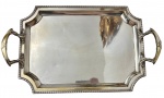 Antiga bandeja em metal espessurado a prata, de formato retangular com cantos recortados, borda cinzelada e alças laterais vazadas ricamente ornamentadas em relevo. Medidas: 6,5 x 51 x 31 cm. Apresenta desgastes.