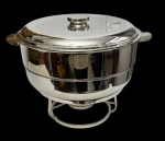 Grande e imponente réchaud em metal espessurado a prata, composta por tampa, recipiente interno removível, suporte para aquecimento e queimador. Corpo de formato circular com alças laterais e acabamento liso. Medidas: 45 x 38,5 x 33 cm.