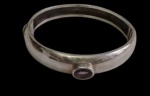 Antigo bracelete em prata, de formato rígido articulado, ornamentado por cabochão em pedra ametista ao centro. Peso: 24,5 gramas. Medidas: 6 cm de diâmetro