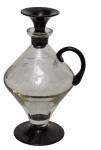 Antiga garrafa em vidro translúcido, com corpo facetado e decoração gravada com motivos vegetalistas, apresentando alça, base e tampa em vidro fumê. Medidas: 22 cm de altura.