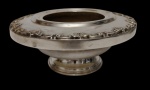 Antiga floreira/centro de mesa em metal espessurado a prata, elevada sobre pé circular, com ampla borda ornamentada em relevo por concheados, volutas e motivos rococó. Medidas: 10 x 26 cm.
