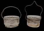 Duas cestas em metal espessurado a prata com recipientes em vidro lapidado, ambas com estruturas vazadas e alças. Medidas: 8 x 10 x 16 cm e 9 x 10 x 12 cm.