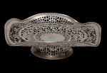 Antiga e imponente fruteira de metal espessurado a prata, marcada, com corpo ricamente vazado em arabescos e centro monogramado, apoiada sobre base circular elevada. Medidas: 6 x 26 cm.