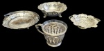 Quatro peças em metal prateado, sendo duas fruteiras vazadas com alças laterais, uma fruteira vazada sobre três pés e uma caneca com suporte e recipiente interno em vidro. Medidas: 8 x 12 cm; 17 x 10 cm; 13 x 9 cm; 6 x 16 cm.