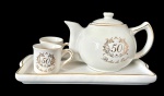 Conjunto comemorativo em porcelana branca decorada, composto por bule com tampa, duas xícaras e uma bandeja retangular, celebração de "50 Anos - Bodas de Ouro". Medidas: prato; 22,5 x 12,5 x 2 cm, bule; 16 x 10 x 10 cm e xícaras; 6 x 4,5 x 4 cm.
