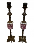 Par de antigos abajures de mesa estruturados em metal decorados com parte central em porcelana com padronagem floral em tons de rosa e roxo. Cada peça apresenta fuste torneado, bocais para lâmpada na extremidade superior e base quadrangular ricamente ornamentada com volutas e relevos. fiação elétrica antiga, sem funcionamento. Medidas: 46 x 10 cm.