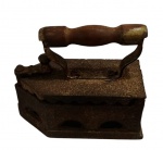 Antigo ferro de passar a brasa, em ferro fundido, com tampa articulada, empunhadura em madeira torneada e aberturas laterais para ventilação e manutenção da brasa. Medidas: 20 x 9 x 19 cm.