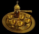 Jogo marroquino em metal dourado, composto por bandeja redonda, bule com cabo lateral e seis copinhos, todos ricamente ornamentados com decoração gravada de inspiração oriental. Medidas: 30 cm de diâmetro (bandeja), 17 x 7 cm (bule) e 5 x 6 cm (cada copinho).