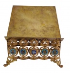 Antigo porta-bíblia de altar em metal dourado, com estrutura vazada ricamente ornamentada por elementos florais e medalhões decorados com aplicações em esmalte policromado representando ícones sacros. Tampo articulado com sistema de regulagem para inclinação, permitindo o ajuste do ângulo de leitura. Apoiado sobre quatro pés recortados de inspiração barroca. Medidas: 33 x 31 x 16 cm.