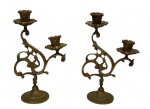 Antigo par de castiçais em bronze, de dois lumes, com hastes vazadas em elegantes volutas e rica ornamentação em relevo, apoiados sobre base circular decorada. Medidas: 24 x 8 cm.