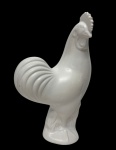 Imponente escultura representando galo, em porcelana branca esmaltada, de modelagem elegante e volumetria acentuada, marcada na base. Apresenta discretíssimo bicado na crista. Medidas: 34 x 20,5 x 11 cm.