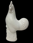 Imponente escultura representando galo, em porcelana branca esmaltada, de modelagem elegante e volumetria acentuada, marcada na base. Medidas: 34 x 20,5 x 11 cm.