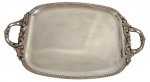 Grande e imponente bandeja em metal espessurado a prata, de formato retangular com cantos arredondados, centro liso e borda cinzelada. Alças vazadas ricamente ornamentadas por motivos vegetalistas e concheados em relevo. Medidas: 35,3 x 59 cm.