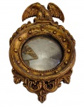 Antigo espelho bisotado de parede,  moldura patinada, ricamente ornamentada em relevo com frisos perolados, volutas e folhas de acanto, encimada por figura de águia de asas abertas, no estilo Império. Apresenta manchas no espelho e uma das asas da águia colada. Medidas: 33 x 20 cm.
