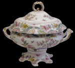 Grande e imponente sopeira em porcelana, com decoração policromada de flores, borboletas e reservas ornamentais em relevo, com filetes dourados. Corpo bojudo sobre pedestal recortado, com alças laterais e tampa encimada por elegante pega vazada. Medidas: 30 x 36 x 25 cm. Manufatura no verso.