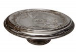 Antiga e imponente fruteira em metal espessurado a prata, elevada sobre pedestal circular. Corpo ricamente ornamentado em relevo, com borda recortada, centro decorado por motivos florais e cartelas em estilo Rococó, apresentando elegante trabalho de cinzelagem. Medidas: 13 x 31 cm.