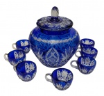 Antiga poncheira em cristal azul cobalto, ricamente lapidada com motivos geométricos e florais, acompanhada de 7 canecas no mesmo padrão. Tampa com pegador facetado e suporte elevado, Medidas da poncheira: 32 x 25 cm. Medidas das canecas: 12,5 x 9 x 7 cm. uma caneca apresenta trincado.