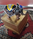 Porta-joias em metal esmaltado, em formato de elefante, com corpo articulado, ricamente ornamentado com aplicações de cristais Swarovski e esmaltação policromada nas tonalidades azul, amarelo, branco e vinho. Medidas: 5 x 12 cm.