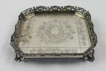 Prata portuguesa, Águia 833, antiga salva de formato qaudrado com centro finamente gravado apresentando cartela envolta por arranjo floral e folhagens, circundado por friso floral. Borda recortada e ricamente vazada, ornamentada por volutas e motivos concheados.  Medidas: 4 x 20 cm. Peso: