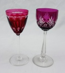Duas taças em cristal na tonalidade rubi, sendo uma ricamente lapidada com motivos geométricos e florais e outra decorada com lapidação em gomos e friso lapidado junto à borda. Uma das taças apresenta quebra na borda. Medidas: 20 x 7 cm e 19 x 7 cm.