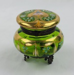 Antigo porta-joias veneziano em vidro verde, com tampo, ornamentado com frisos em ouro e delicados motivos florais esmaltados. Guarnições em metal com três pés de apoio de desenho ornamental. Medidas: 9 x 10 cm.