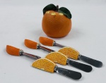 Conjunto porta-petiscos em resina, em formato de laranja, composto por recipiente esférico e 6 espátula com cabos modelados em gomos de laranja. Medidas: 14 x 9 cm