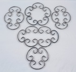 Cinco descansos de panela em metal prateado, com estrutura vazada formada por volutas, de desenho ornamental. Medidas: 17 cm a 35 cm.