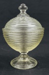 Compoteira / Bombonière em vidro prensado, com corpo esférico ornamentado por frisos concêntricos, tampa com pegador e base pedestal. Medidas: 18 x 12 cm. Apresenta pequenos bicados.