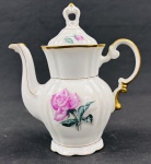 Real. Bule em porcelana esmaltada, decorada com motivo floral representando rosas, com filetes dourados e alça ornamentada. Marca da manufatura na base. Medidas: 18 x 16 cm.