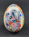 Grande ovo decorativo em porcelana esmaltada, ricamente decorado em policromia com aves, flores e paisagem oriental, apresentando ornamentação floral e geométrica com detalhes dourados. Medidas: 22 cm de altura.