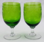 Par de taças em demi cristal verde, com bojo ornamentado por delicada decoração gravada em motivos florais e arabescos, haste e base transparentes. Medidas: 14 x 7 cm.
