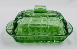 Antiga manteigueira em vidro verde prensado, composta por base e tampa, ornamentada em relevo com padrão geométrico de losangos. Medidas: 9 x 17 x 11cm.