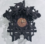 Relógio de parede cuco, em madeira entalhada e patinada, ricamente ornamentado com folhas de videira, cachos de uva e ave em vulto no frontão. Mostrador circular em madeira com algarismos romanos em relevo e ponteiros em metal vazado. Apresenta ausência dos pesos. Medidas: 56 x 45 cm. Não testado, sem garantias de funcionamento.