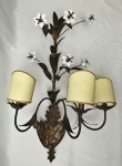 Antiga arandela de parede para três luzes, em metal trabalhado com rica composição floral em relevo, apresentando hastes curvas, folhas estilizadas e delicadas flores aplicadas em opalina branca. Cúpulas em tecido no tom bege. Medindo; 75 x 40 cm.