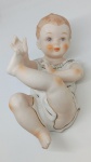 Bela e delicada estatueta de bebê em porcelana, em posição deitada. Bom estado geral, apresenta avaria em um dos pés . Mede 24 cm