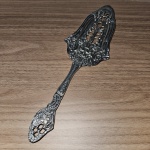 Antiga espátula para bolo, com design clássico com detalhes em relevo e arabescos, floral, em metal prateado, Mede 23x7 cm.