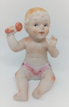Bebê em biscuit , com 12 cm de altura, em pose sentada e segurando brinquedo. Peça delicada, com pintura em tons suaves.