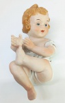 Figura infantil em biscuit, com 15 cm de altura, em pose sentada e com delicados detalhes de pintura.