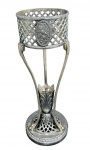 WMF - Württembergische Metallwarenfabrik, Geislingen an der Steige, Alemanha(Fundada em 1853) - Elegante suporte para floreira em metal espessurado a prata alemã. capitel fenestrado com bordas lavradas cm sulcos horizontais e fitas cruzadas, circundado por três longas pernas curvilíneas, encimadas por volutas cobertas por acantos, e terminadas com pés de garra, centro cinzelado com palmetas. Base circular, de centro vazado, contornada por faixa relevada com flores imbricadas. Apresenta marcas da manufatura ao fundo. Perdas no banho. Medindo 32 x 11 cm