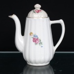 Bule para café em porcelana nacional, produção de meados do século XX, com corpo bojudo de perfil canelado, colo estreitado e base circular. Bico vertedor alto, alongado e recurvado, com extremidade recortada; alça lateral estilizada, ligada à região superior e inferior do recipiente. Tampa ligeiramente abaulada, rematada por pomo cônico. Decoração composta por flores em tonalidades de amarelo, rosa, branco e azul, entre folhagens verdes, distribuída na face principal e repetida em menor escala no reverso e sobre a tampa. Contornos superiores, tampa e pomo realçados por frisos em douradura. Medidas: Alt.: 18 x Comp.: 17 x Larg.: 9,5cm.