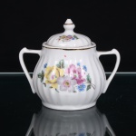 Porcelana Pozzani, Jundiaí - SP (Fundada em 1934 por Francisco Pozzani). Açucareiro em porcelana nacional, produção de meados do século XX, com corpo bojudo de perfil canelado, colo estreitado e base circular, alças laterais estuilizadas, tampa abaulada, rematada por pomo cônico; decoração floral em estampagem policromada, composta por rosas e flores em tonalidades amarela, rosa, azul, branca e verde. Contornos superiores, tampa, pomo e alças realçados por frisos em douradura. Marca de manufatura Pozzani Jundiaí na base. Medidas: Alt.: 10 x Comp.: 11 x Larg.: 8cm.