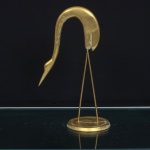 Escultura decorativa representando garça, executada em bronze e latão dourado. Ave de perfil, com pescoço longilíneo acentuadamente recurvado, cabeça reduzida e bico longo e afilado. Estrutura sustentada por duas hastes delgadas em latão, fixadas sobre base circular escalonada. Composição de linhas simplificadas, sem representação de plumagem. Medidas: Alt.: 24 x Comp.: 15 x Larg.: 9cm.