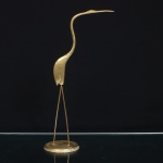 Escultura decorativa representando garça, executada em bronze e latão dourado. Figura de perfil, constituída por corpo alongado de contornos simplificados, pescoço esguio em acentuada curvatura sinuosa, cabeça integrada ao prolongamento cervical e bico longo e afilado disposto horizontalmente. Pernas representadas por duas hastes delgadas em latão, fixadas sobre base circular escalonada. Composição de caráter modernista. Medidas: Alt.: 34,5 x Comp.: 17 x Larg.: 9,5cm.