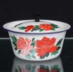 Panela em metal esmaltado, de corpo circular, borda revirada, acompanhada de tampa abaulada com puxador central preto. Superfície revestida por esmalte branco, ornamentada com composições florais policromadas, constituídas por flores em vermelho e rosa entre folhagens verdes. Boca e tampa delimitadas por filete azul-cobalto. Motivos florais repetidos sobre a cobertura. Marca circular Li Guan  Enamel in China na base, acompanhada do número 06. Medidas: Alt.: x Diam.: