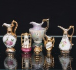 Conjunto de seis(06) miniaturas decorativas em porcelana. Composto por pequenos jarros e ânforas de diferentes formatos, com corpos globulares, piriformes e ovóides, providos de alças e bicos vertedores. Decoração executada em policromia, com motivos florais, reservas e revestimentos de efeito nacarado, complementados por extensas aplicações de douradura. Uma das peças apresenta inscrição manuscrita. Circa 19501970. Medidas: