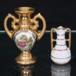 Duas ânforas miniatura em porcelana, um  de corpo ovóide sobre pé circular, colo cilíndrico e duas alças vazadas de desenho vegetalista, apresenta superfície dourada e reserva frontal policroma com cena galante, delimitada por cercadura de motivos fitomórficos em ouro; base numerada 83. O outro, de corpo piriforme, apresenta duas alças verticais, esmaltação branca, filetes horizontais em vermelho e violeta e realces dourados nas alças e no bordo. Medidas: Alt.: 8 x Comp.: 6 x Larg.: 3,5cmMedidas: Alt.: 5,5 x Comp.: 3 x Larg.: 2,5cm.